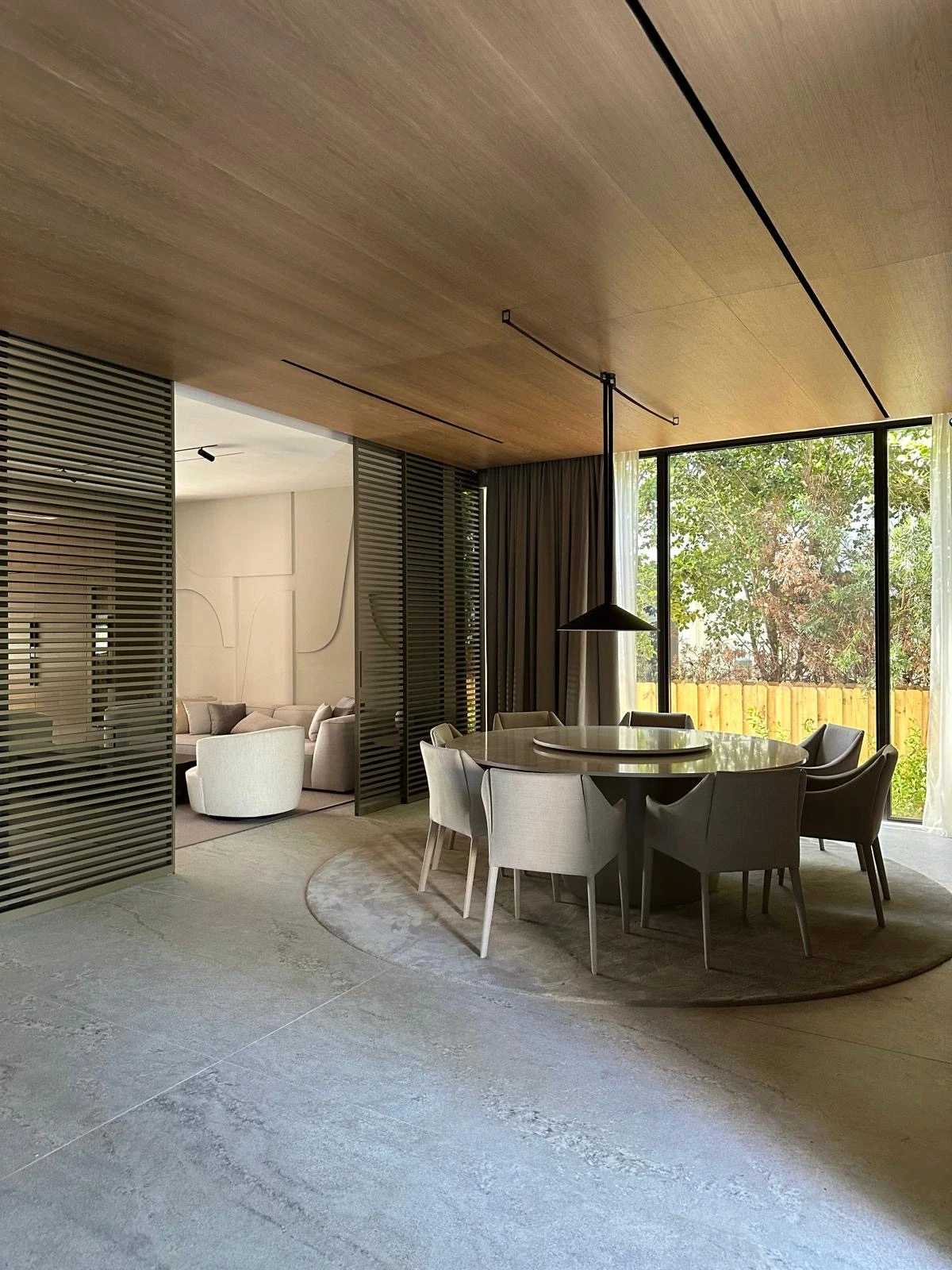 Dining room at the Meridian Avenue Residence in Miami Beach, designed by Atelier International, with a timber-clad ceiling, round table, and full-height glazing onto the garden.