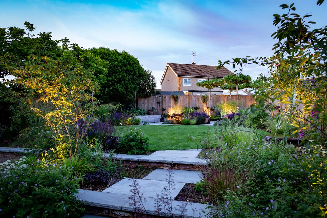 A serene landscape featuring a house surrounded by greenery, with a pond reflecting the sky in the foreground.