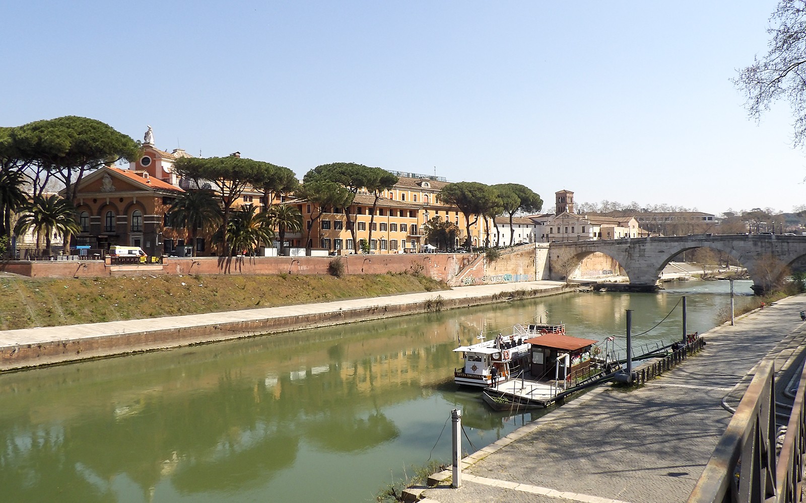 在羅馬的台伯河上停靠的隨上隨下的河船，靠近歷史建築和一座石橋。