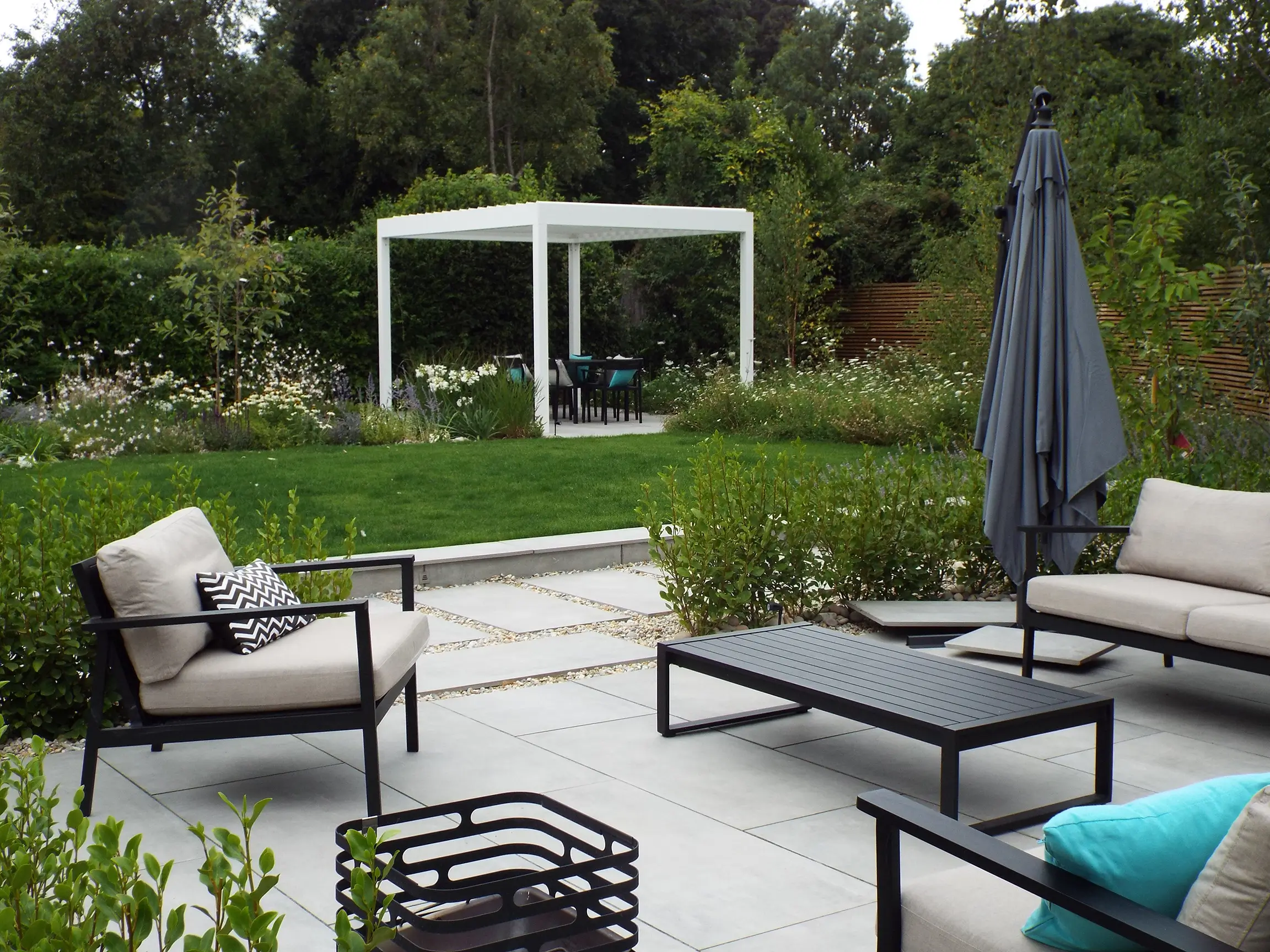 A serene patio area with comfortable seating, greenery, and a white pergola in the background.