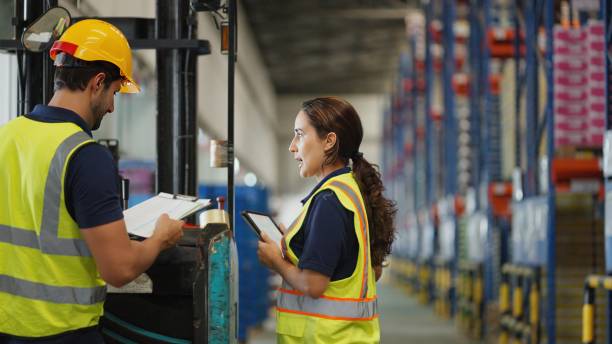 two people wearing high vis vest looking at paper work in a warehouse