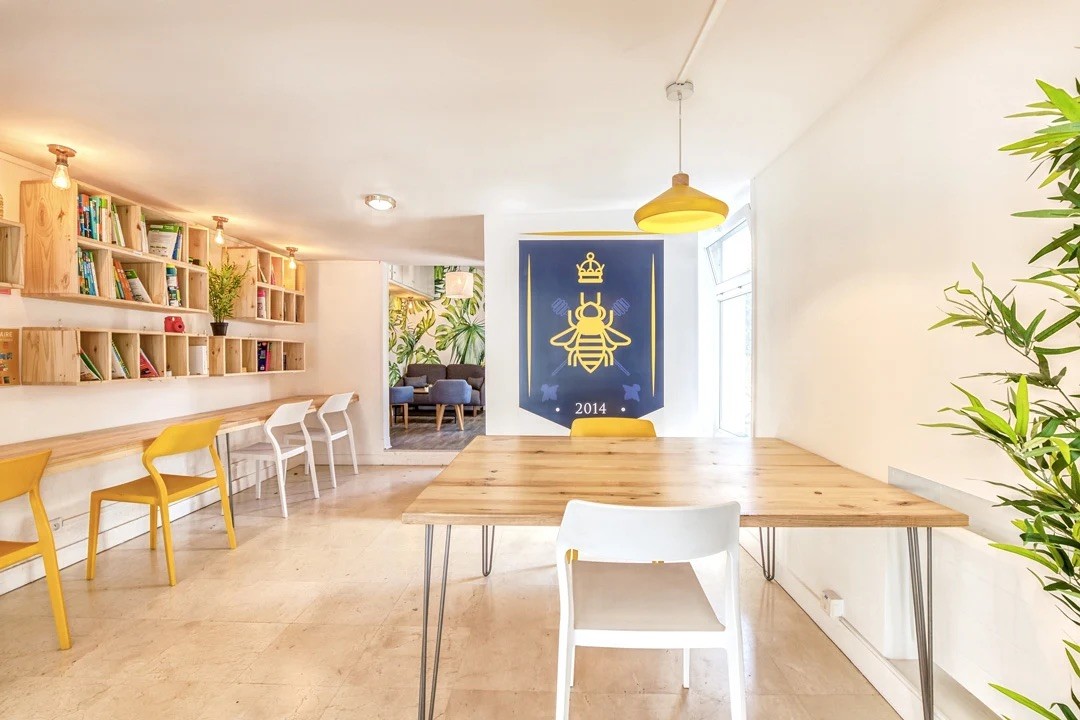 Zone de détente avec bibliothèque sur-mesure en bois clair, chaises jaunes et décoration murale artistique.