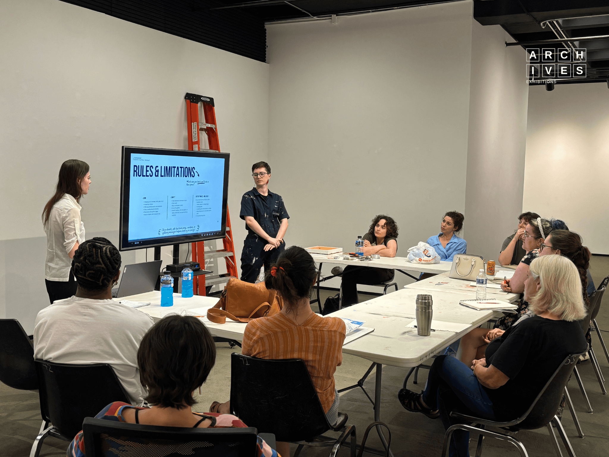 Emma Sonnier and Lex R. Thomas giving a workshop about surviving install to a group of artists in a gallery