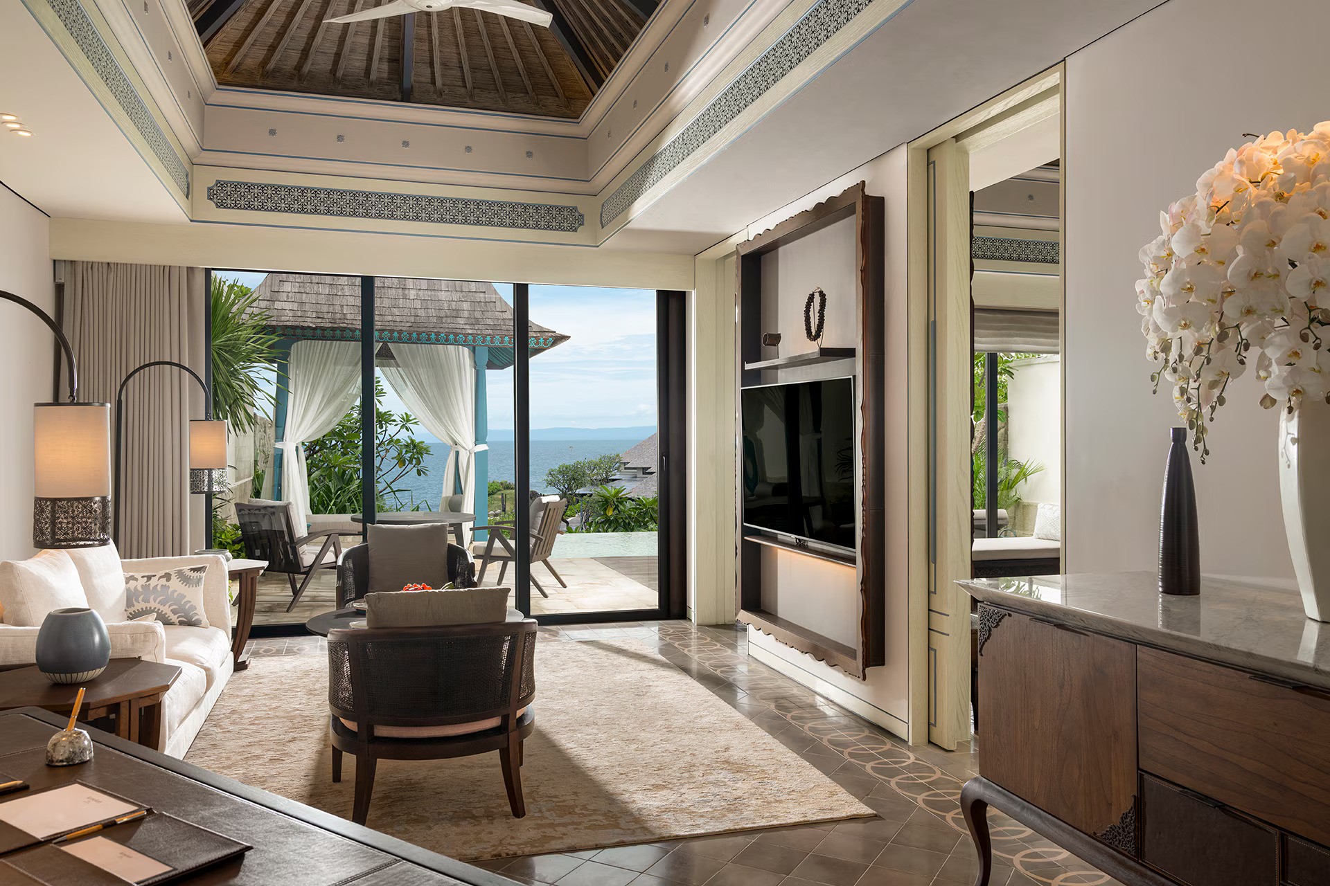 View of the French countryside through a stone villa’s open living room, with sofas and trees framing the scene