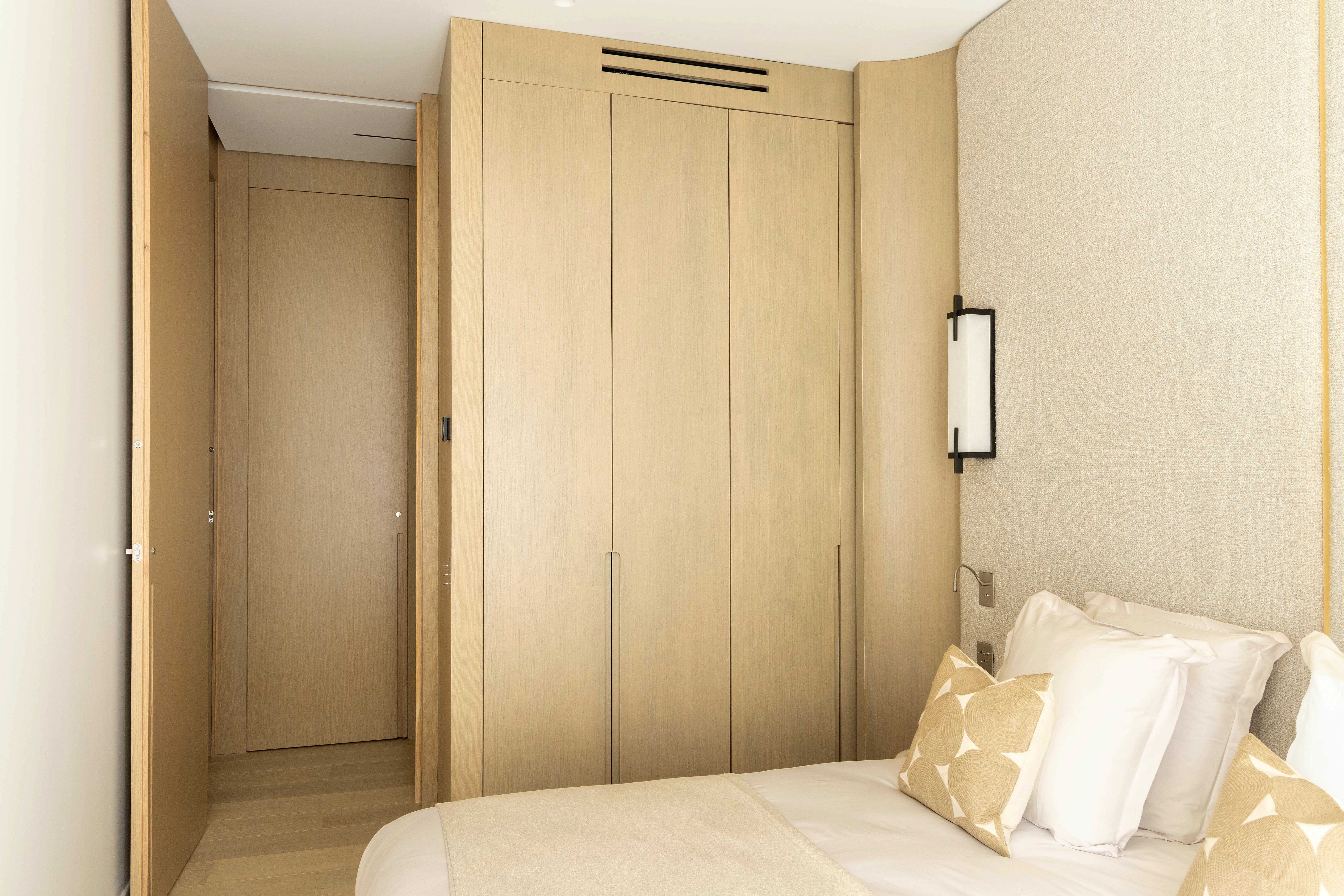 Seconde chambre avec penderie en bois clair, applique murale et lit aux coussins graphiques beiges