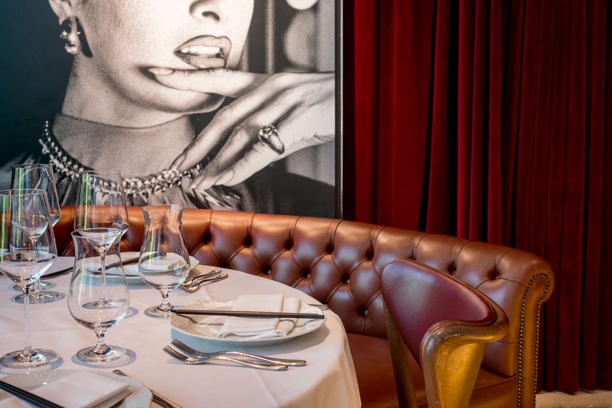 A set table with white linens and glassware in front of a leather booth and a large black-and-white portrait mural.
