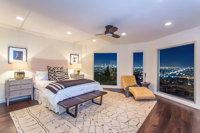 Aerial view of a small neighborhood with red-roofed houses nestled among lush green fields and winding roads. The scene feels peaceful and idyllic.