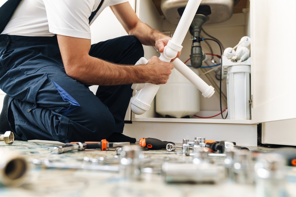 A plumber taking apart some pipes, tools are on the ground next to him