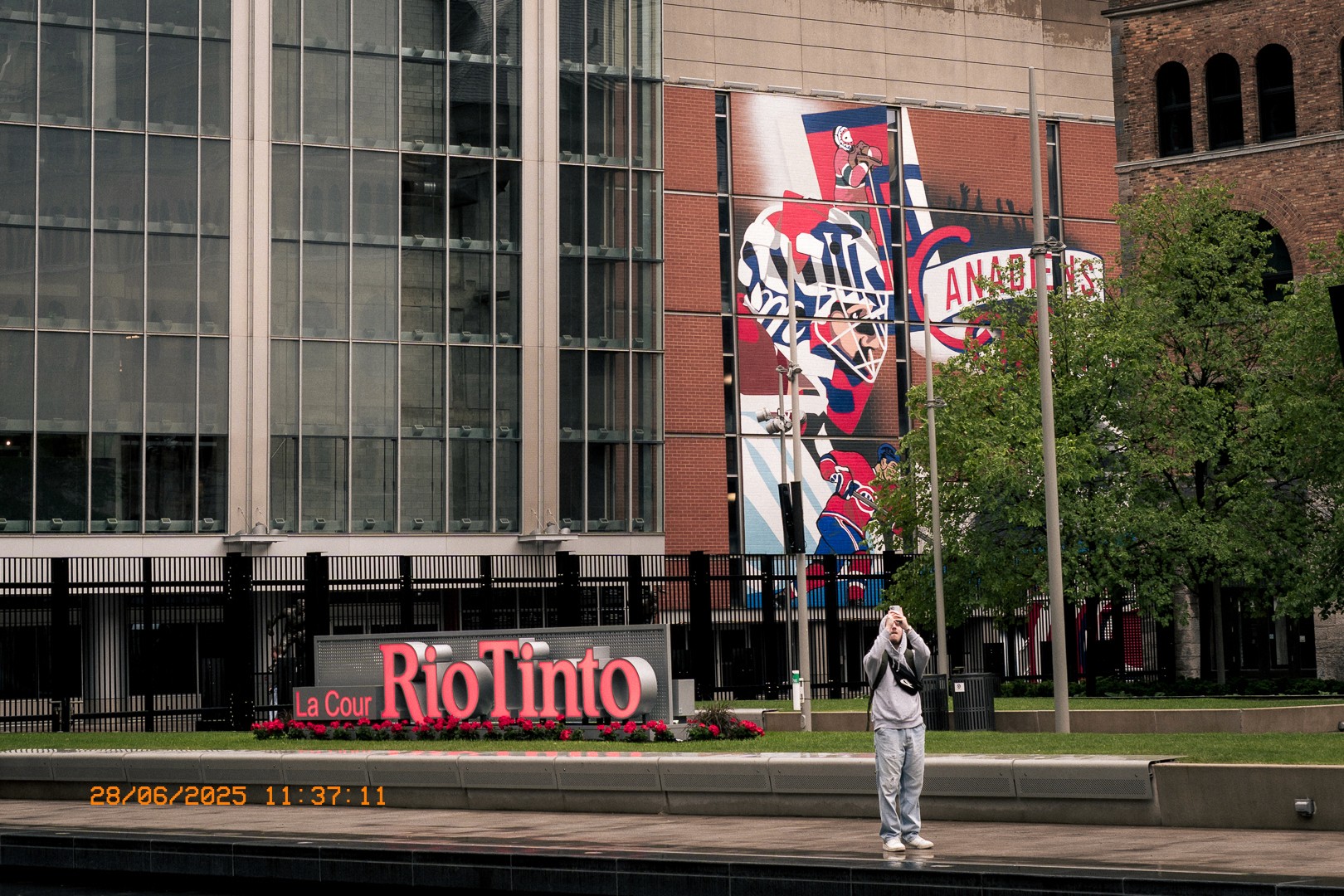 Jeune homme prenant une photo devant la Cour Rio Tinto et le Centre Bell.