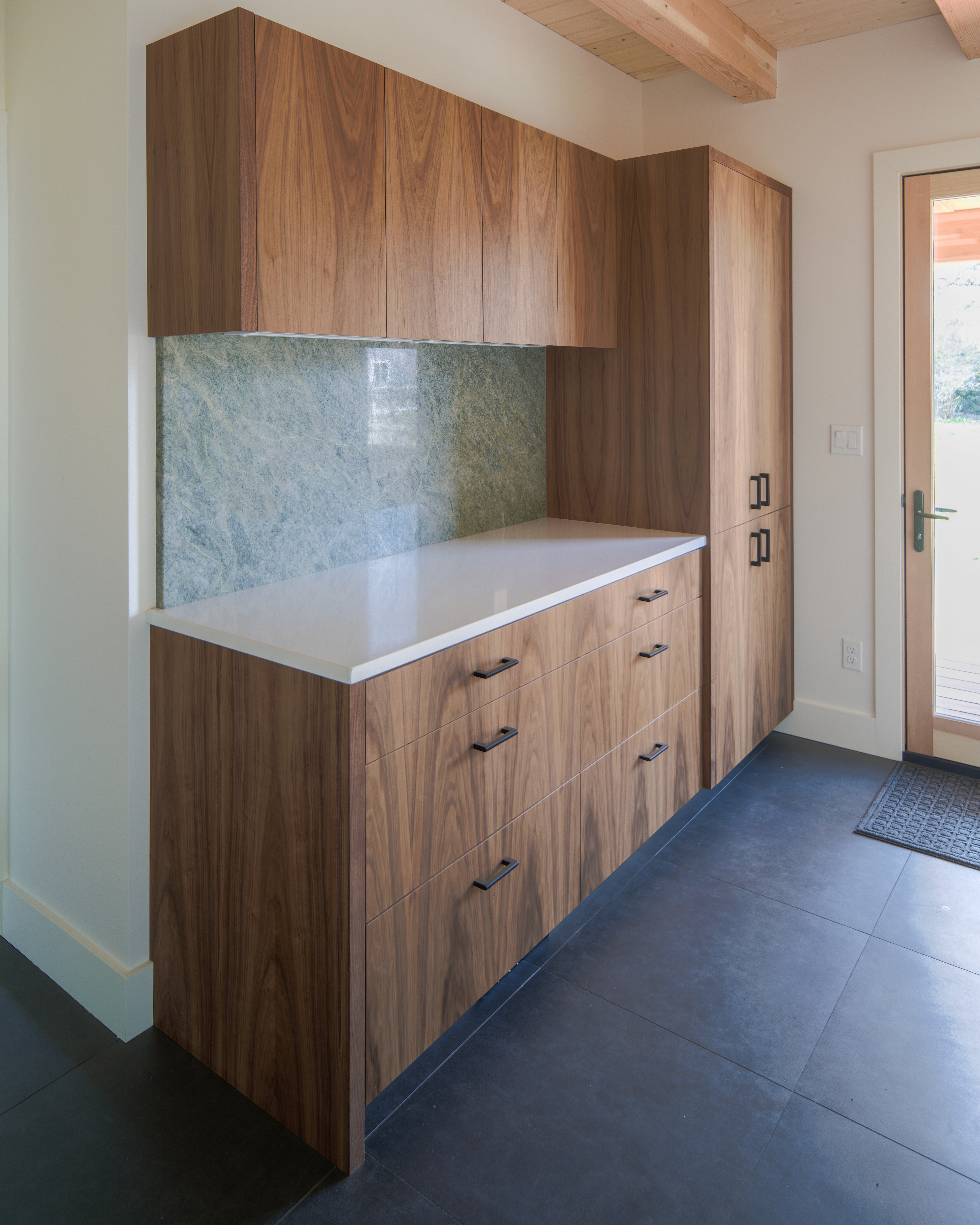 Wood kitchen cabinets with a white countertop and green backsplash sit next to a wood built-in pantry.