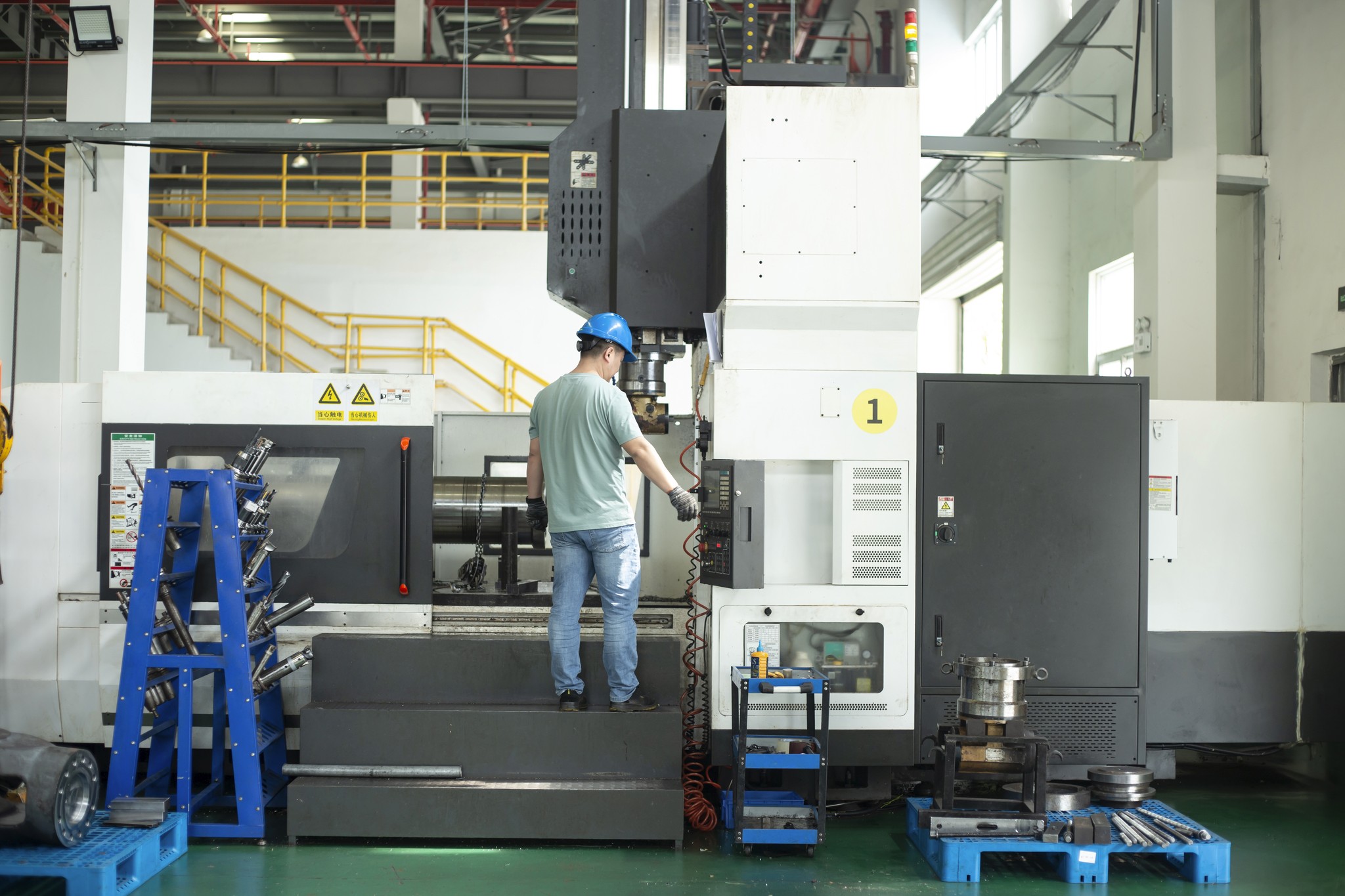 Worker operating CNC machine for aftermarket mining parts.