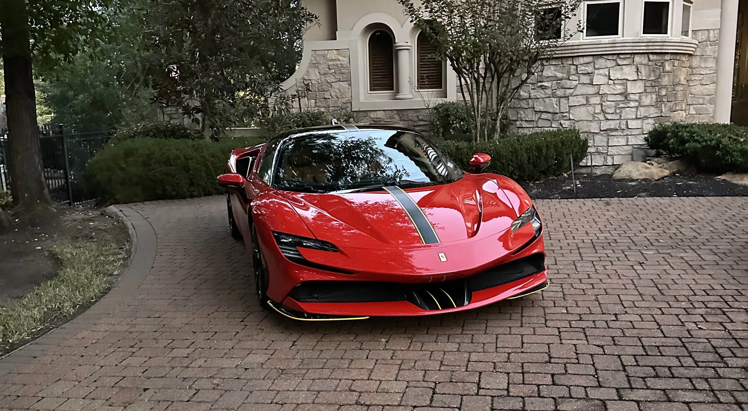 A red Ferrari SF90 Stradale with a black center stripe parked on a brick driveway in Houston after receiving a high-end exterior detail.