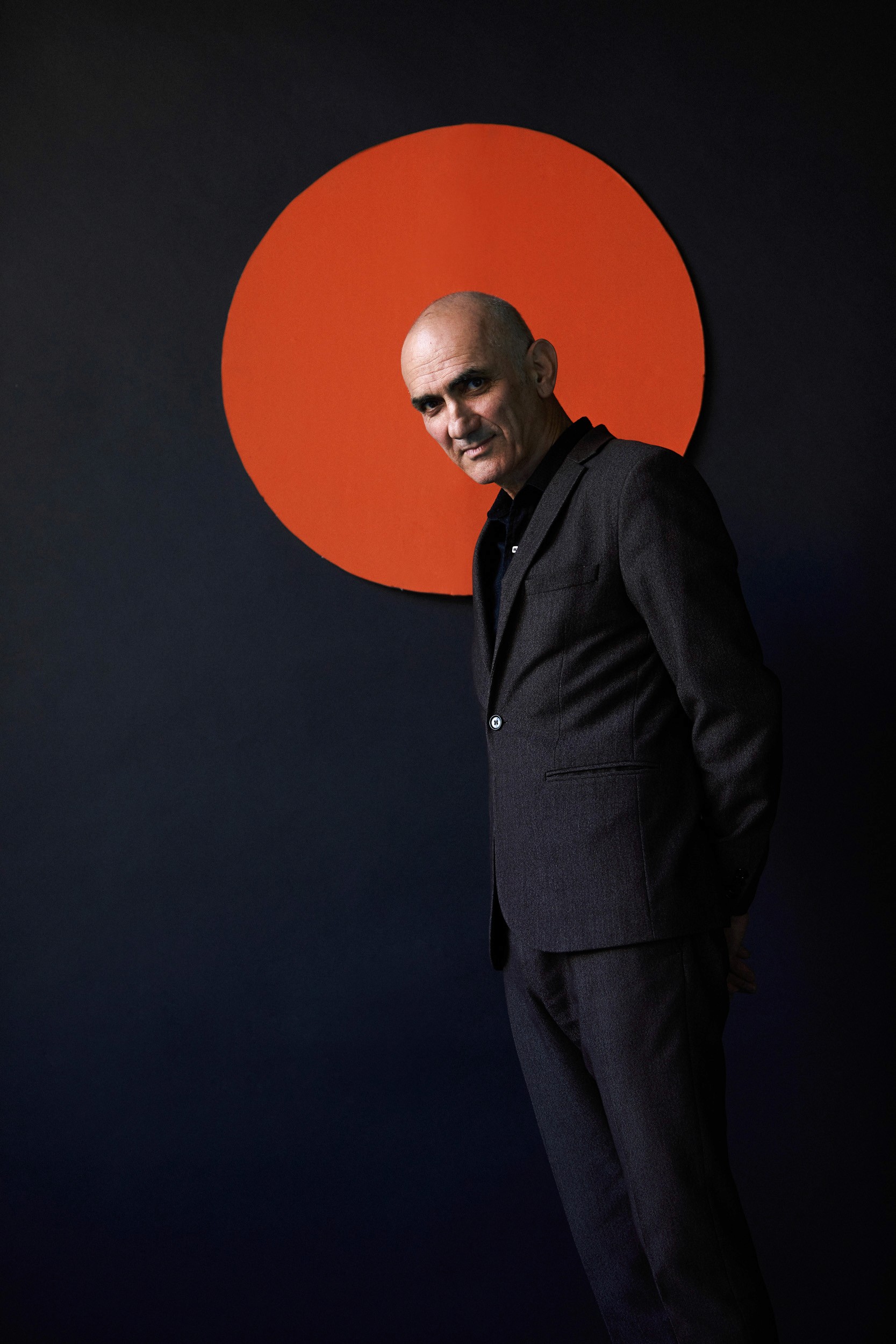 Editorial portrait in Sydney by photographer Cybele Malinowski, featuring a man in a dark suit against a navy backdrop with a bold orange graphic circle. paul kelly universal photoshoot