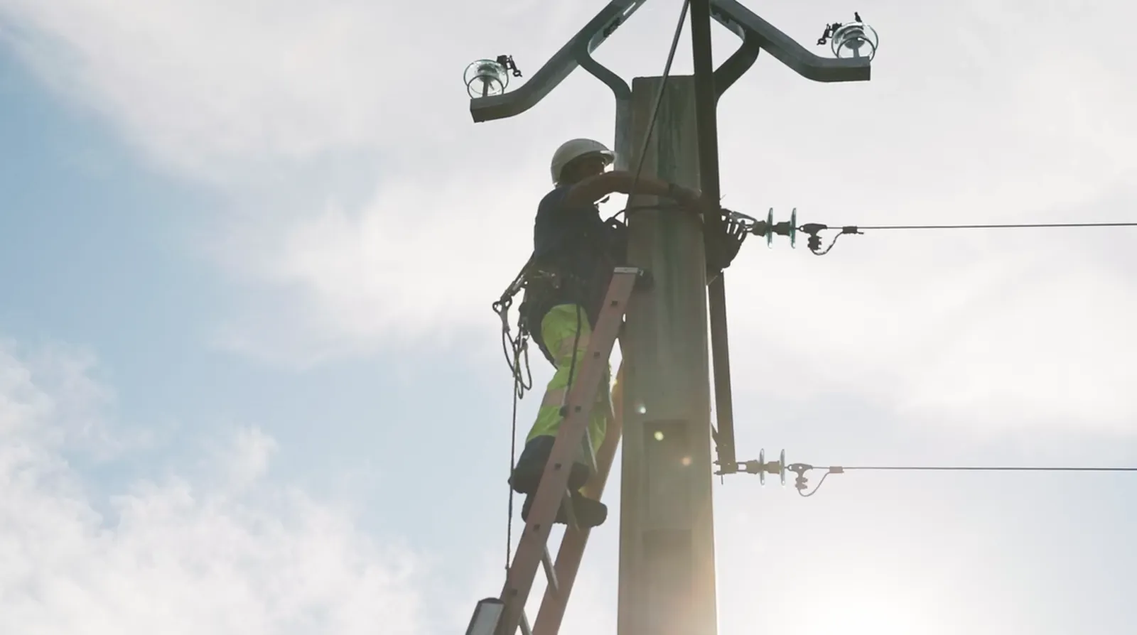 Technicien électricien en gilet jaune sur échelle intervenant sur un poteau électrique haute tension