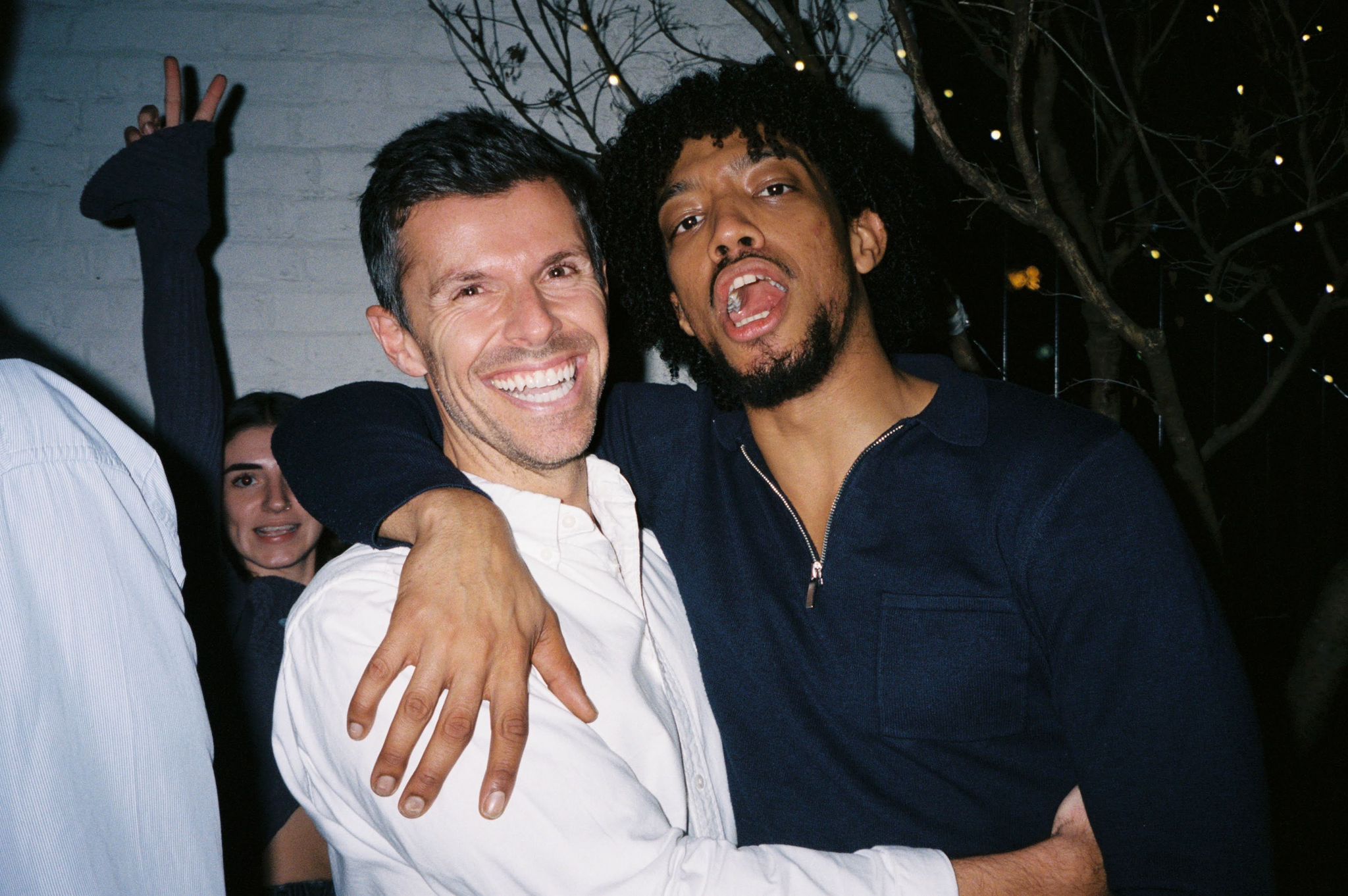 Two smiling men pose closely together at a social gathering, with festive decorations in the background.