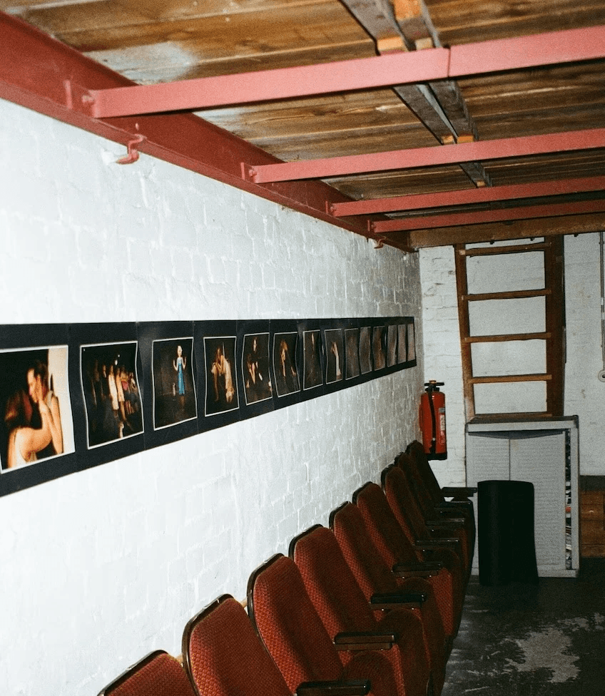 Eine Reihe alter Kinosessel lehnen an einer Wand an der eine Reihe von Fotos hängt.