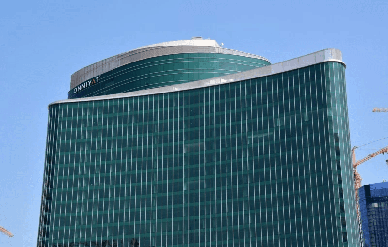The Binary by Omniyat, a prominent city building featuring a striking green glass facade amidst urban surroundings.