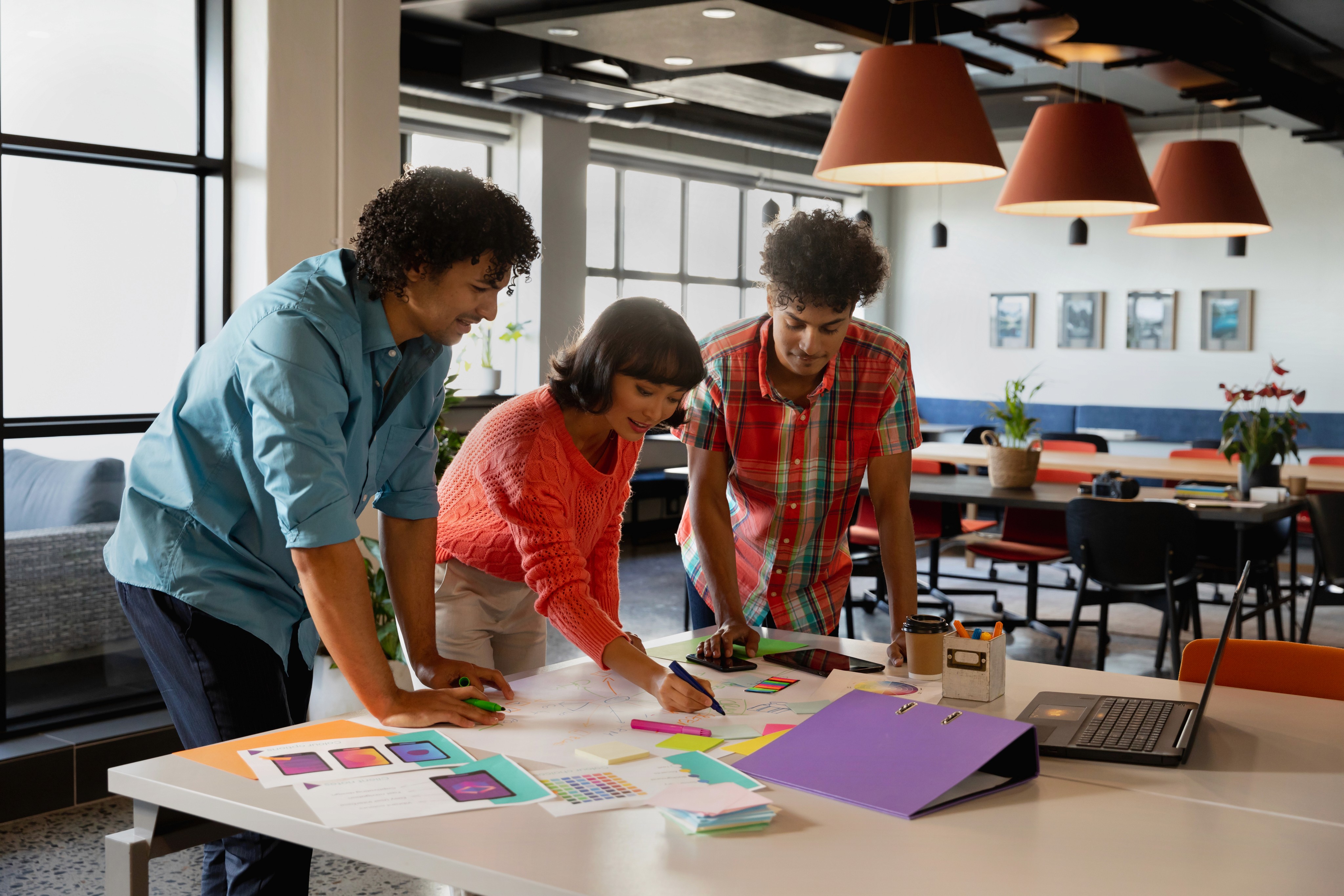 Three young designers collaborating over sketches and color samples at a table in a modern office.