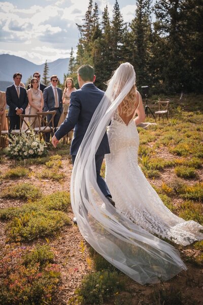 The bride's long veil catches the light as the couple walk past their wedding guests.
