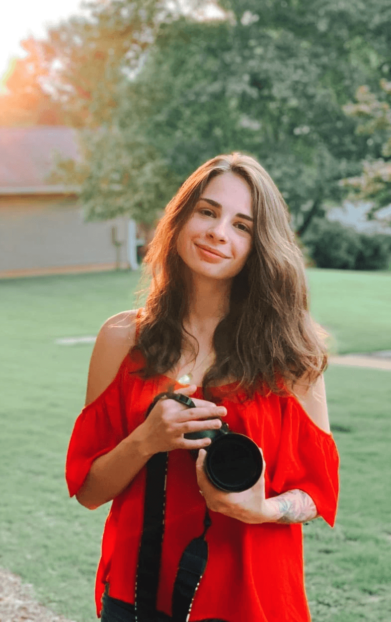 A person with short blonde hair holds a vintage camera.