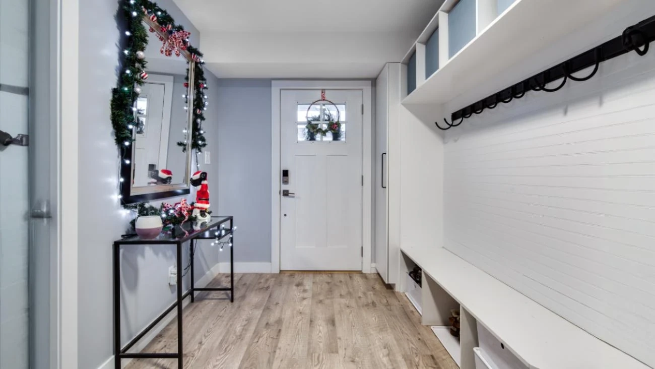 Bright custom home mudroom with white shiplap accent wall, built-in bench seating, organized coat hooks, and light wood-look vinyl plank flooring in Burnaby family home