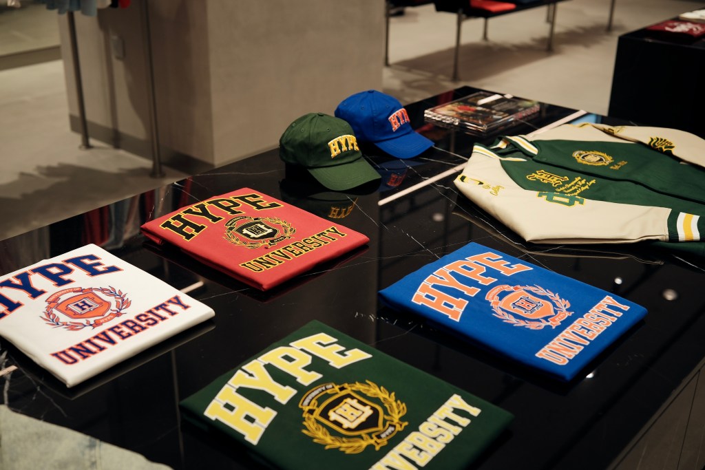 A display of colorful apparel featuring 'HYPE UNIVERSITY' printed on various t-shirts and caps, arranged neatly on a black table in a clothing store.