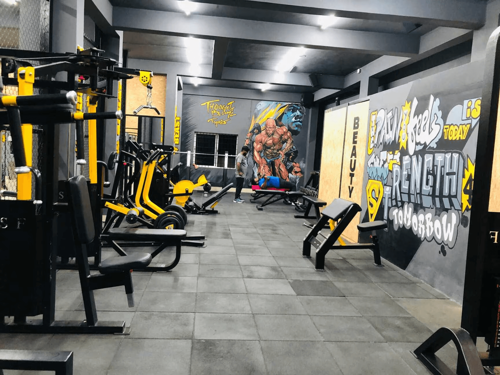 A spacious gym featuring various yellow and black workout machines and equipment, well-lit with smooth flooring.