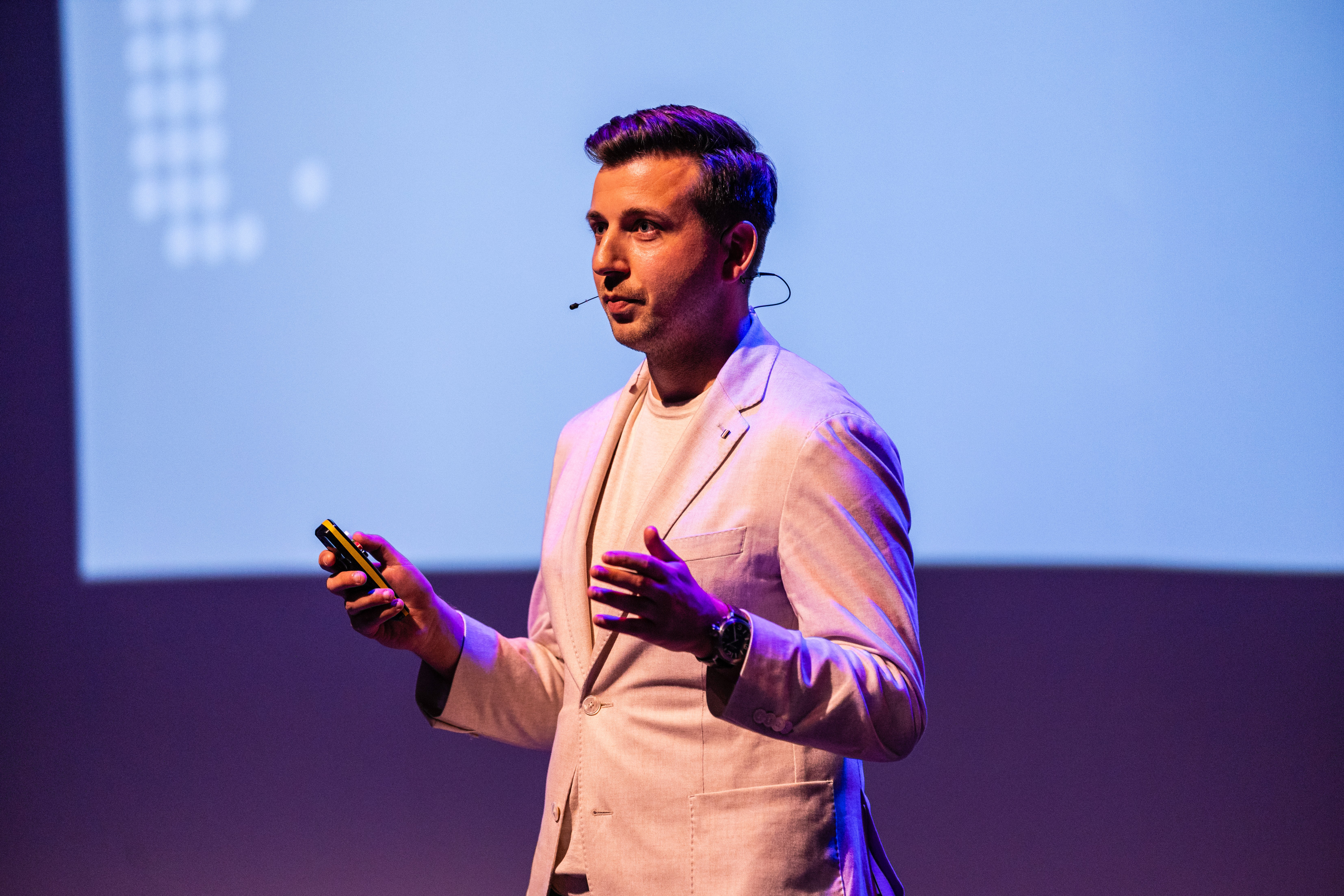 Smiling young woman with long hair standing against a dark green background, holding a finger to her chin.
