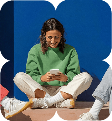 a brown woman with short hair wearing a light green color shirt, cream color pant and white sneakers with white socks smiling when looking at her phone