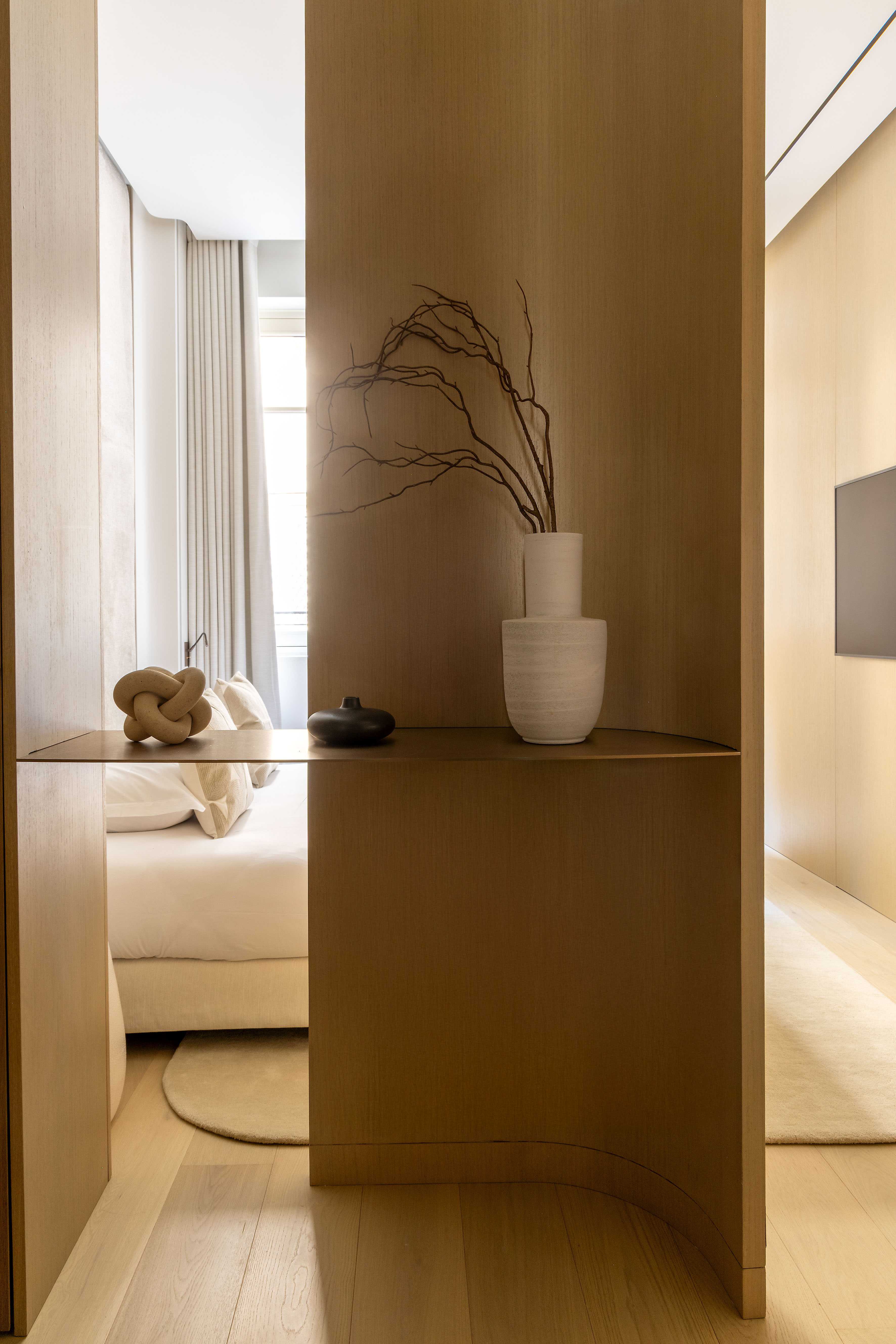 Claustra en bois clair séparant le lit de l'espace TV avec vase en céramique et branches décoratives