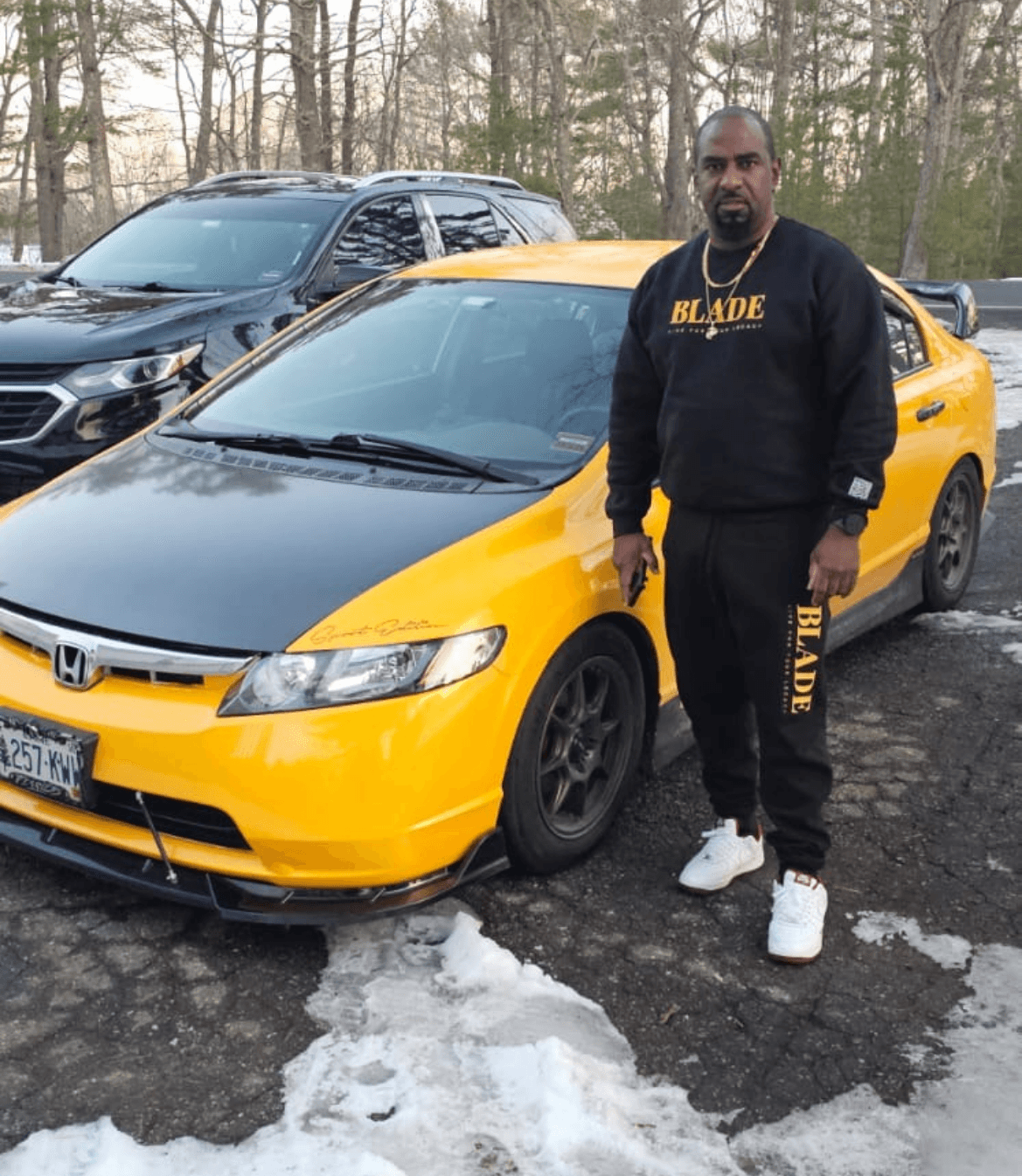 Anthony Hudson wearing a Blade Infiniti tracksuit beside a yellow sports car.
