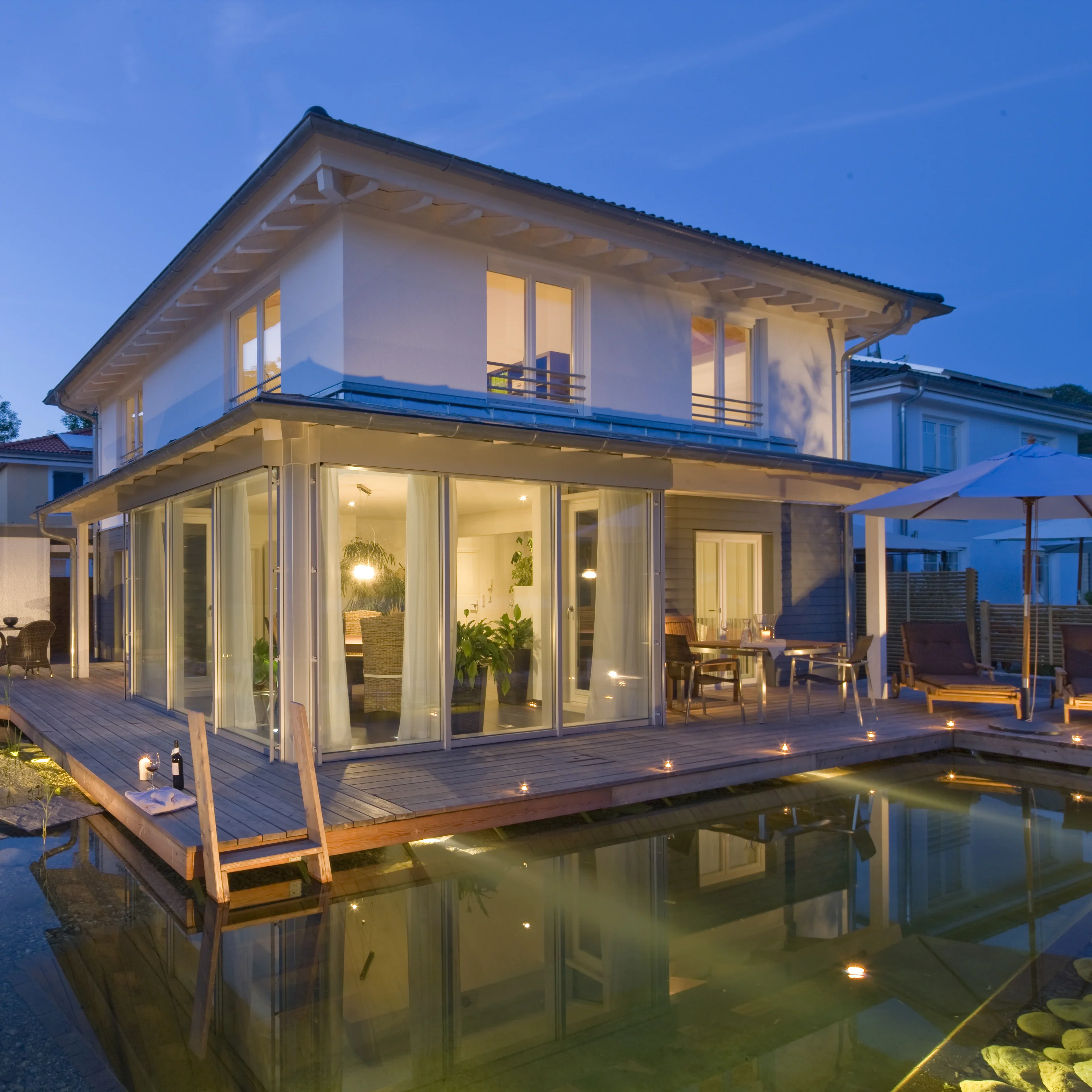 Modernes Haus mit Holzterrasse und beleuchtetem Teich am Abend, L Chasende, Loungebereich mit Sonnenschirm