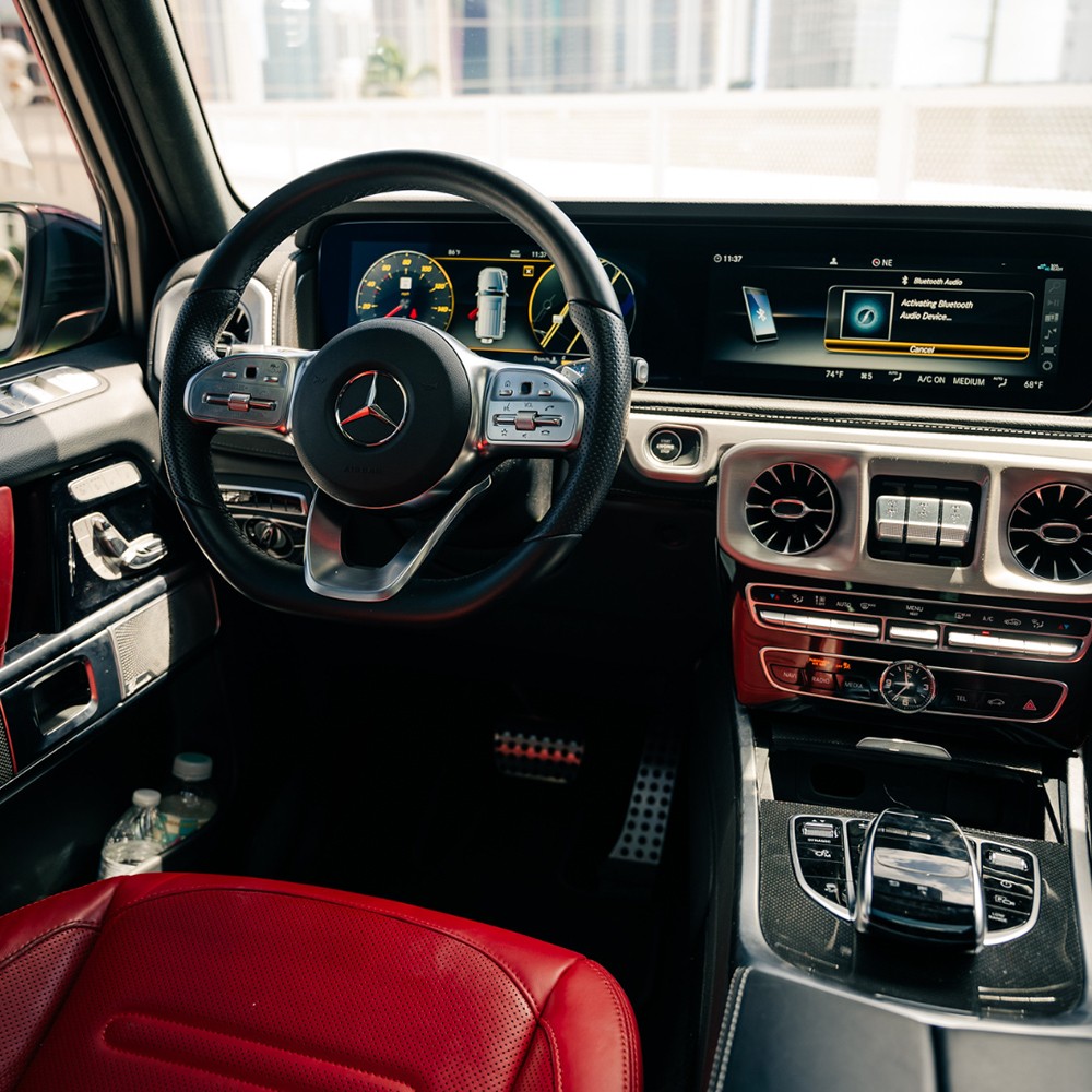 Driver's cockpit of the Mercedes-Benz G 550, featuring a vibrant red leather interior and modern digital displays.