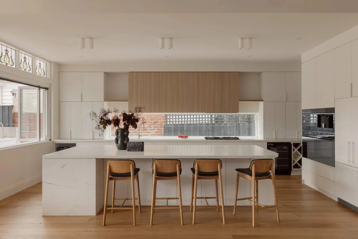 Modern kitchen with white cabinets, marble island, wooden bar stools, and contemporary decor.
