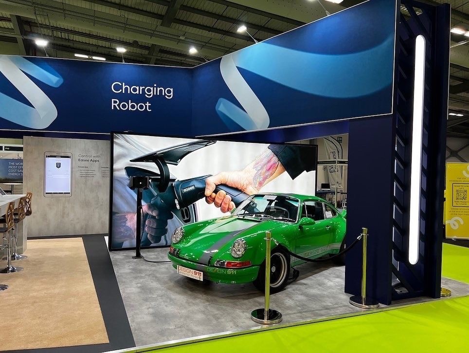 Modern home office setup with a monitor, ergonomic chair, keyboard, and indoor plants near a window with blinds.