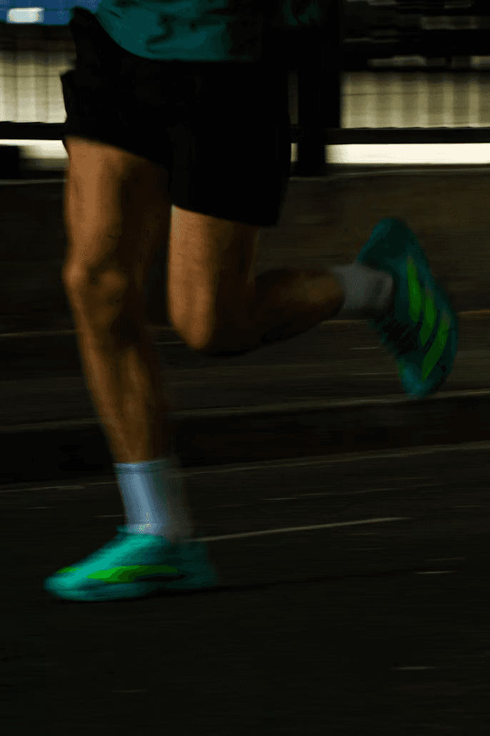 A person runs in bright green shoes and white socks, with a blurred background indicating motion.