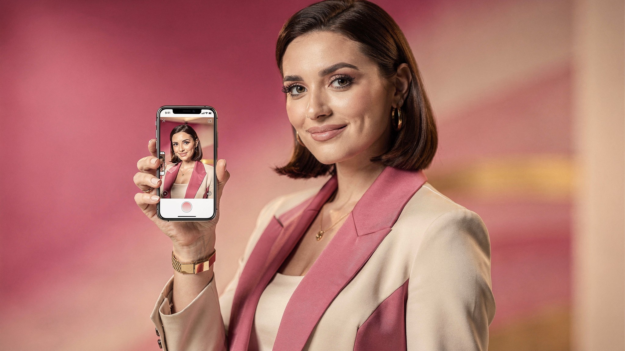 Creator holding her phone showing a polished photo of herself, looking pleased