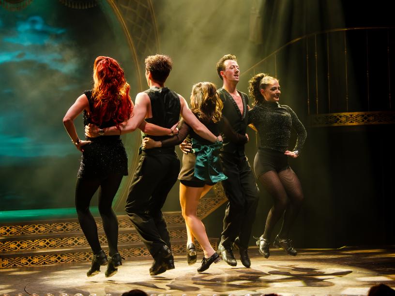 Five dancers performing a powerful jump sequence onstage in Emerald Storm.