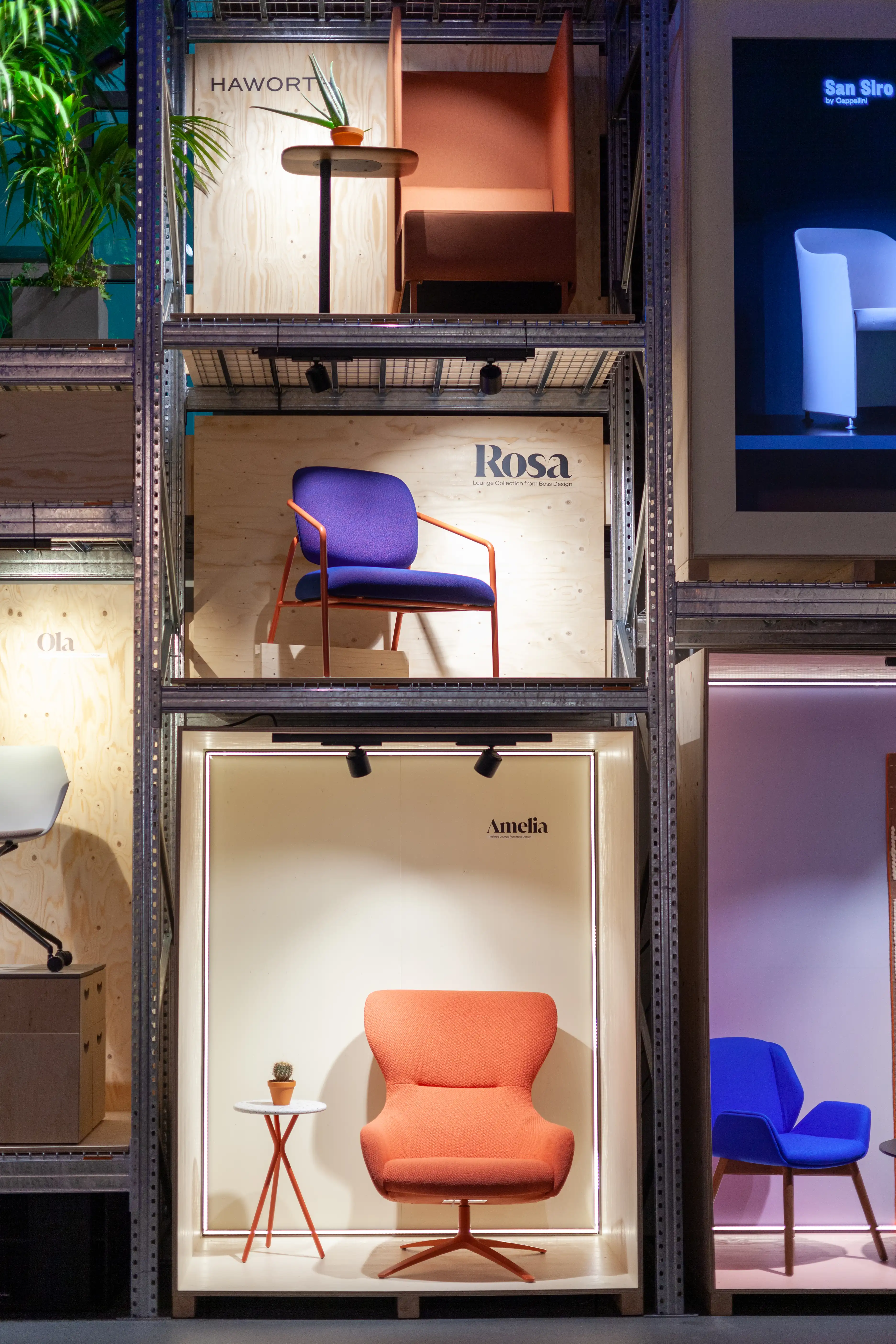 Scaffold shelf at the HAWORTH ORGATEC stand displaying armchairs in lit plywood boxes with brand labels like Rosa and Amelia.