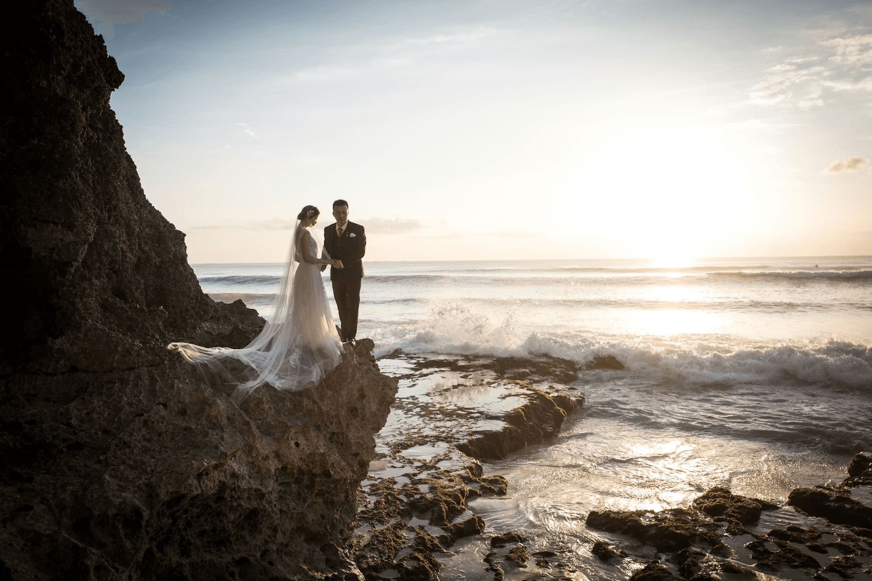 A bride and groom standing on a rocky cliff