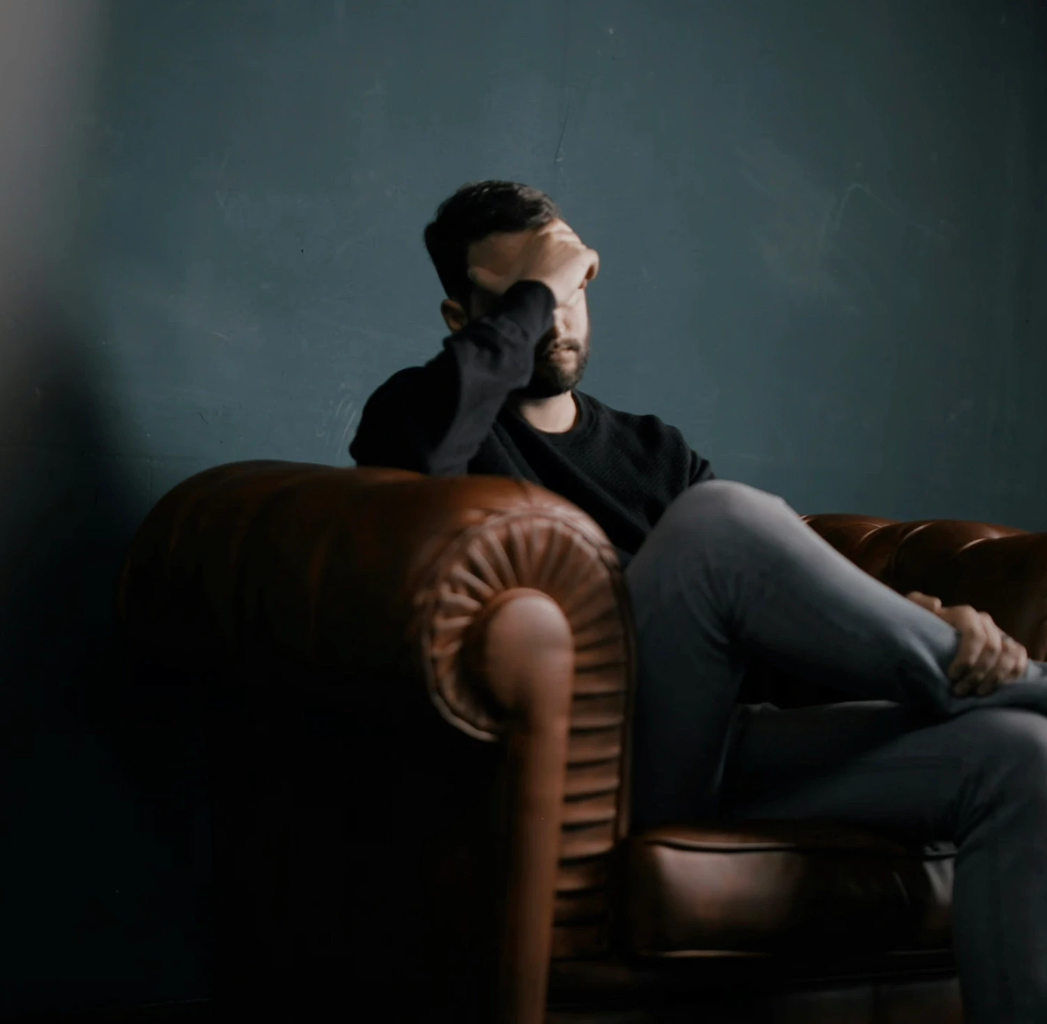 Man sitting on a leather couch with head in hand, symbolizing stress and the need for anxiety therapy in Los Angeles