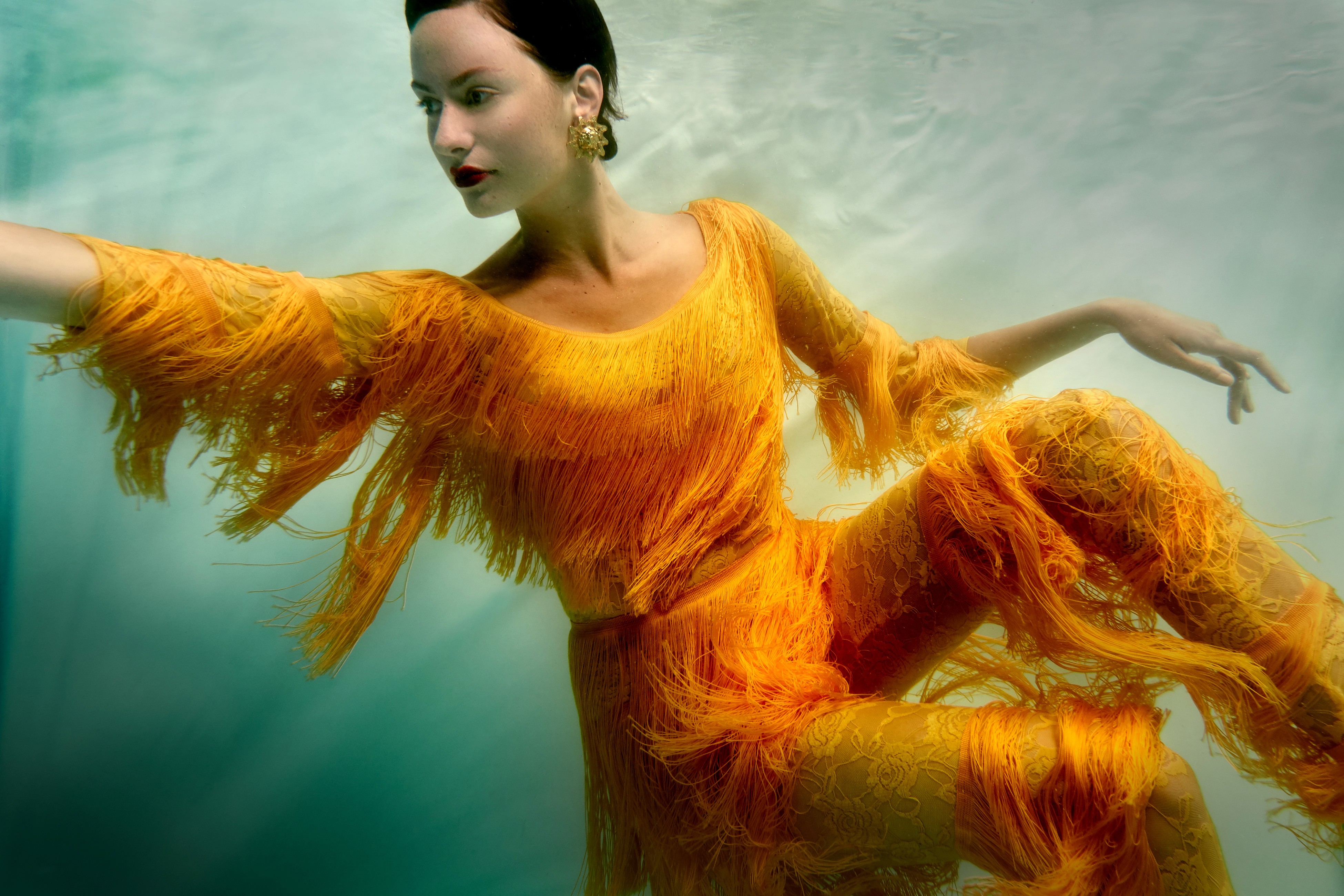 Underwater fashion photography of a model suspended in green water and wearing a stringy yellow two-peice suit.