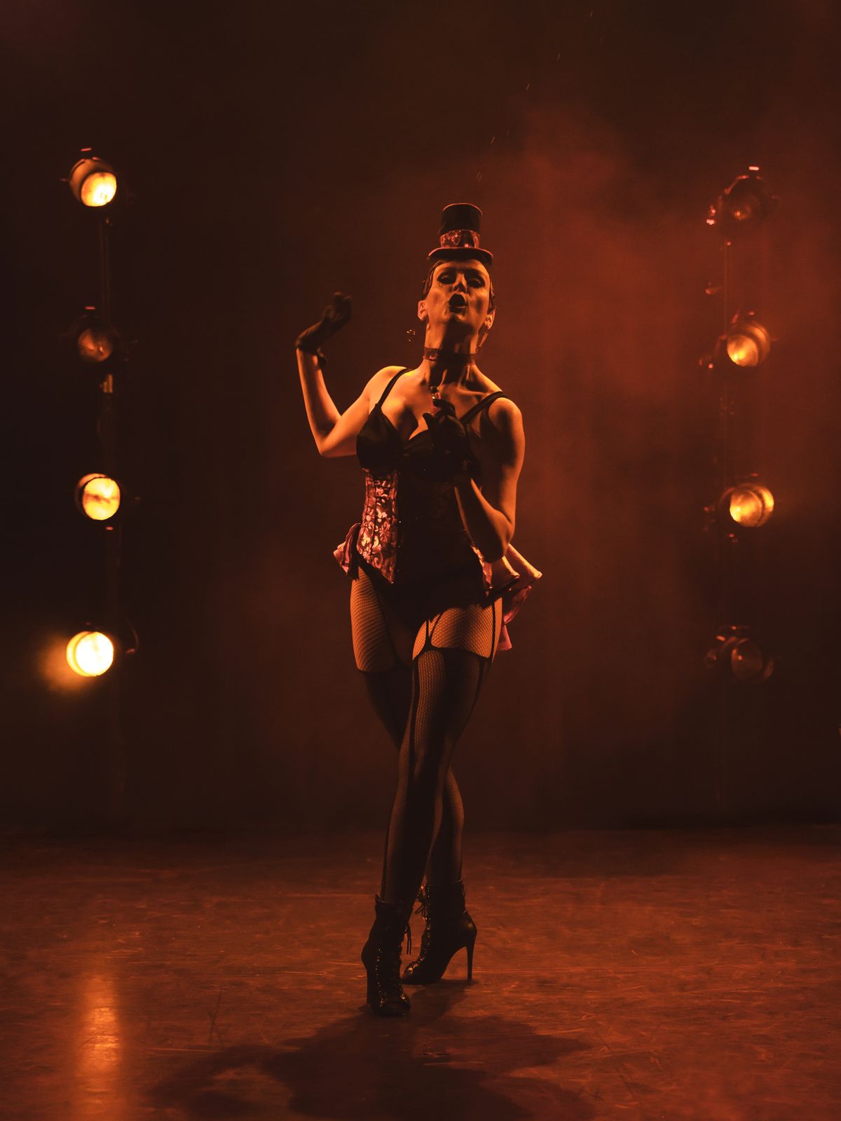 Une artiste en corset et haut-de-forme danse entre des rampes d'ampoules ambrées