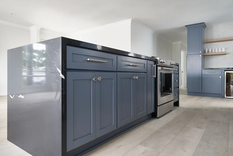 Elegant kitchen corner featuring navy cabinetry, sleek handles, and high-end appliances. Light streams in, complementing the soft wall tones. Photo by Todd Huge.