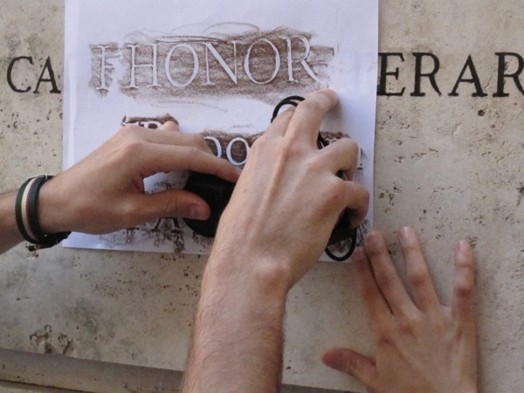 A person copying on a piece of paper some engraved writings from a wall.