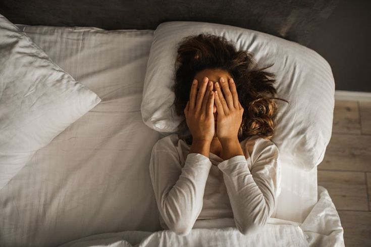 Woman lying in bed with hands covering her face, showing stress and difficulty sleeping.