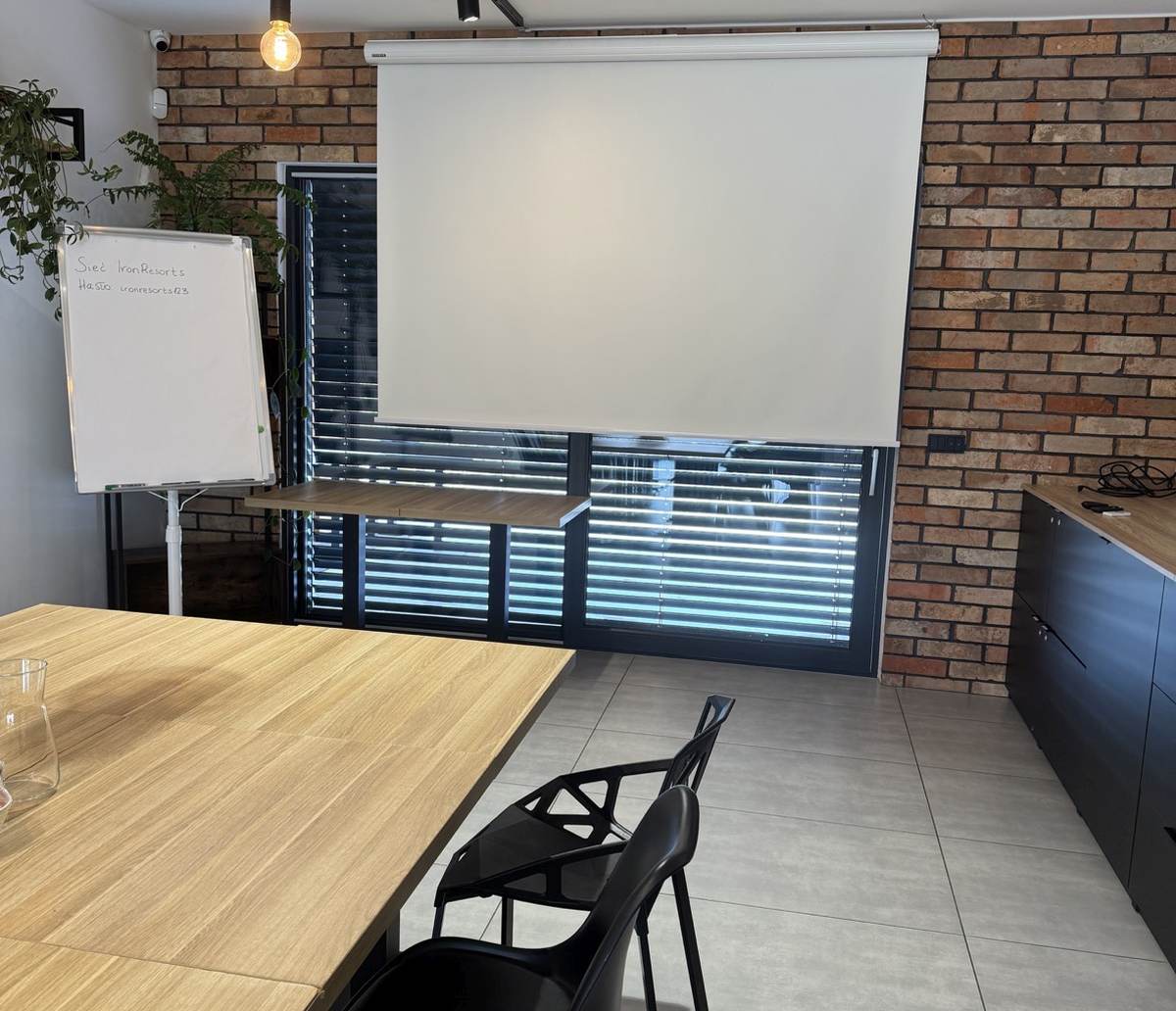 Ekran, flipchart i stół w kameralnej sali warsztatowej