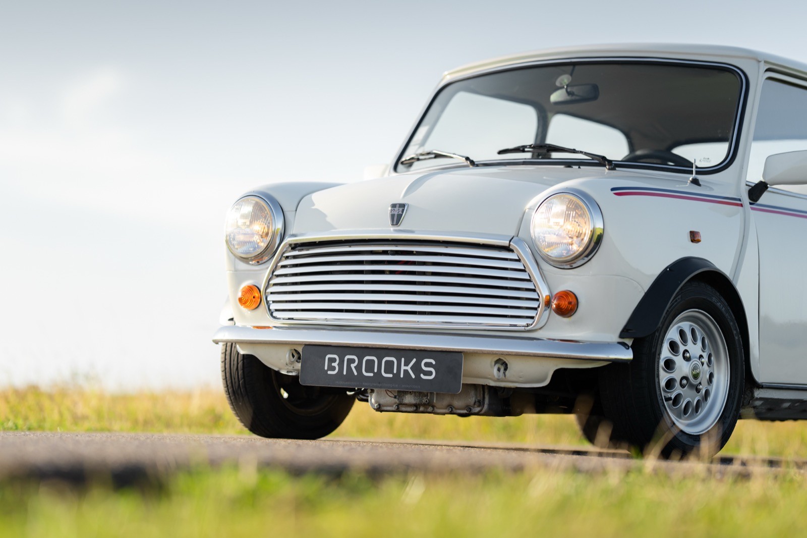 A classic white car parked on a grassy landscape under a clear sky, showcasing its vintage design.