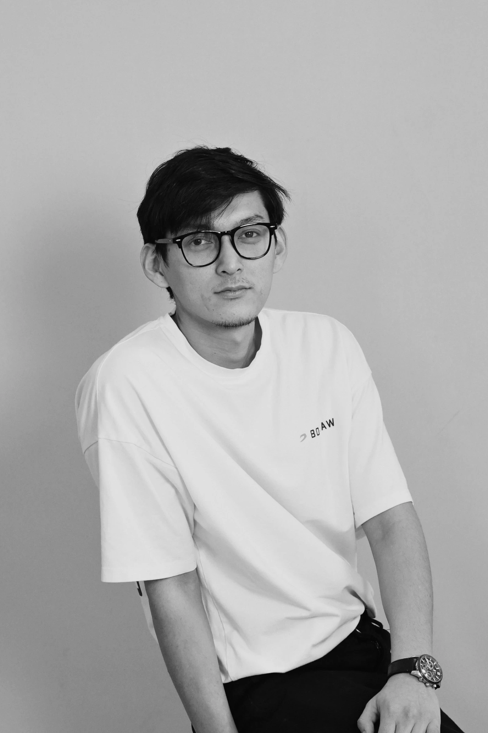 A man reading from a tablet in a collaborative office environment. Desks with documents and a discussion between colleagues are visible in the background.