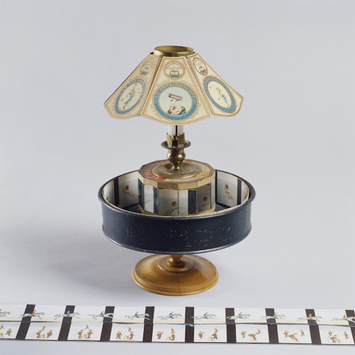 Un zootropo vintage en un soporte con tiras de papel ilustradas que muestran una secuencia de imágenes, presumiblemente para crear visuales animados.